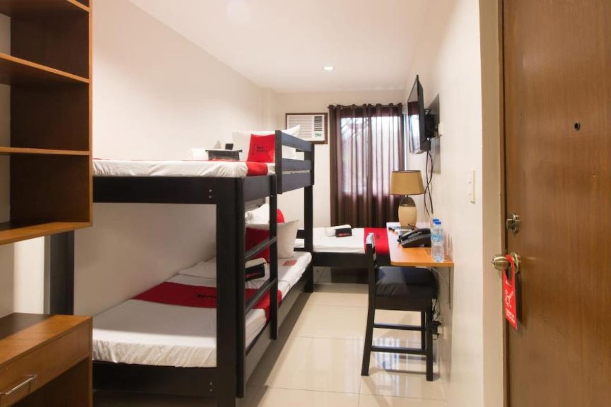 Habitació d'hotel petita amb lliteres, escriptori, cadira, televisió i una porta.