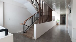 A modern interior with a wooden staircase, white walls, and a hallway leading to an exit. - RedDoorz Plus @ Diola Villamonte Bacolod (Bacolod)