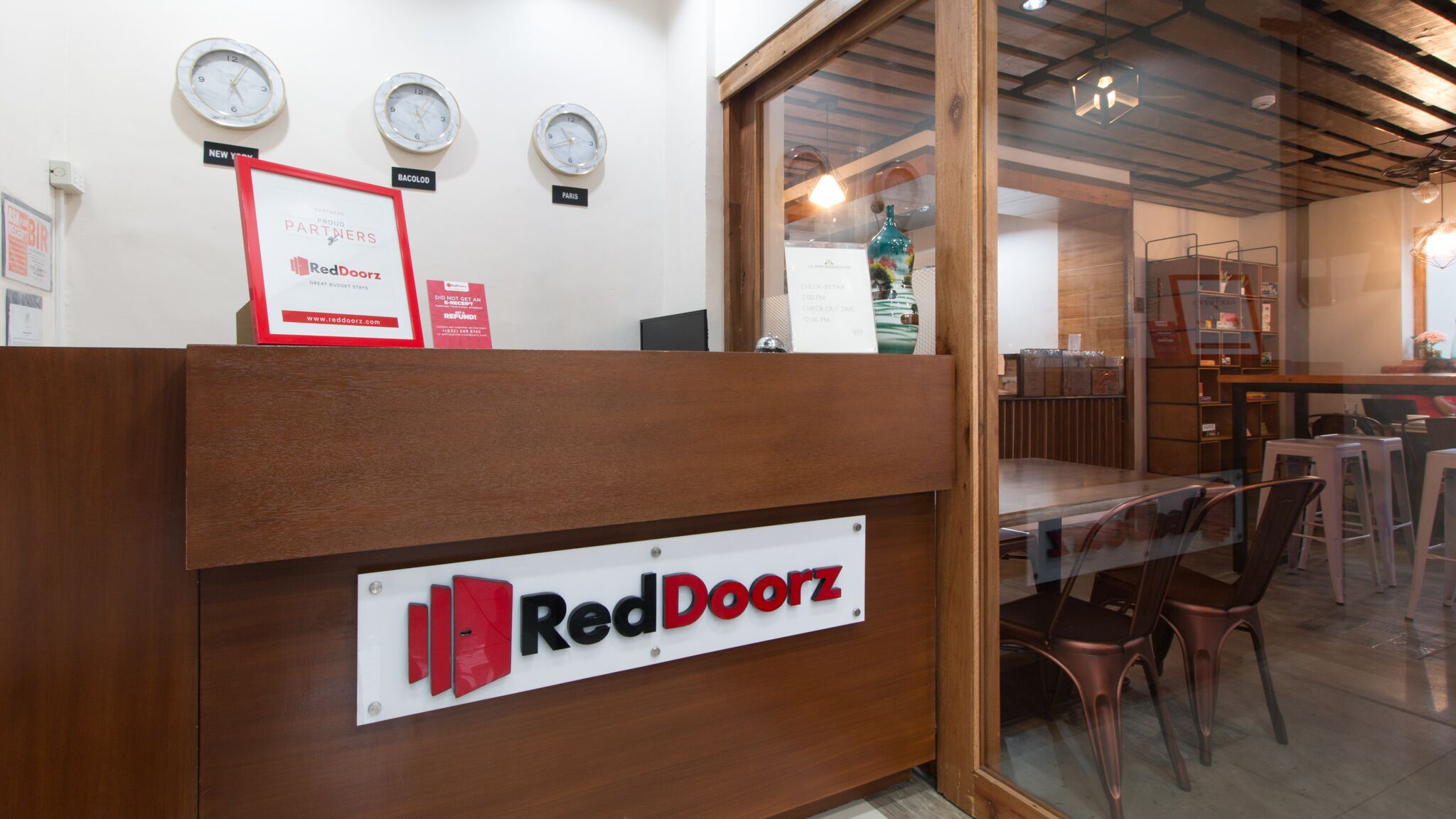 A reception desk with a sign reading "RedDoorz" and clocks labeled "New York," "Bacolod," and "Paris."