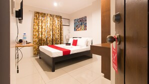 A hotel room with a bed, a desk, a water bottle, a lamp, and a painting on the wall. - RedDoorz Plus @ Diola Villamonte Bacolod (Bacolod)