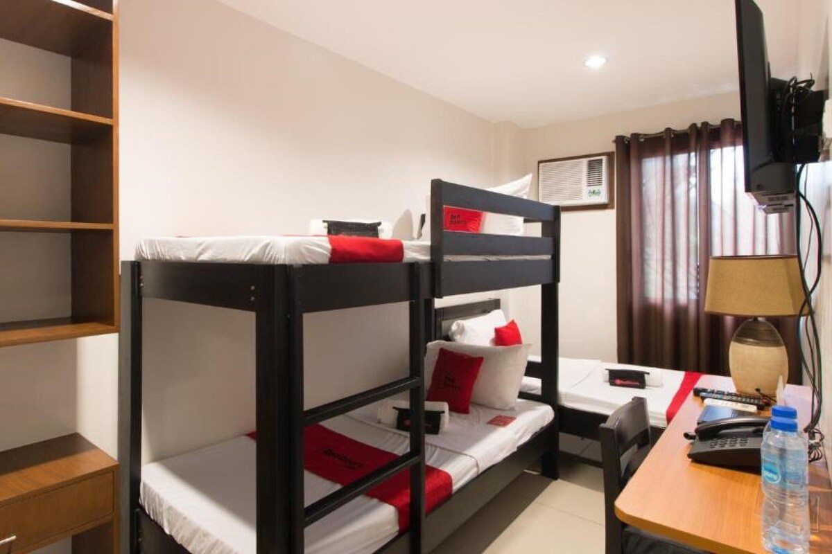 A bunk bed room with a desk, a chair, a lamp, and a television.