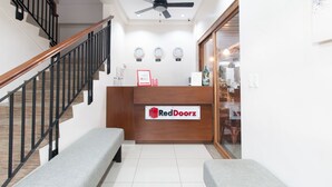 A reception area with a wooden desk, a bench, a staircase with black railings, and a ceiling fan. - RedDoorz Plus @ Diola Villamonte Bacolod (Bacolod)