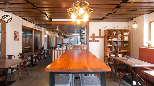 A restaurant with a long wooden counter, multiple seating areas, and a bookshelf filled with books. - RedDoorz Plus @ Diola Villamonte Bacolod (Bacolod)