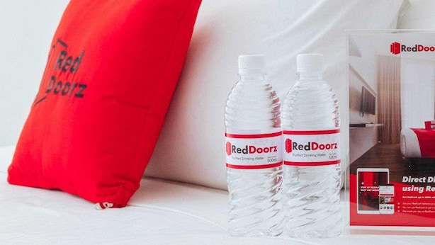 Une chambre d’hôtel avec un oreiller rouge, deux bouteilles d’eau RedDoorz et une brochure RedDoorz.