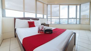 A hotel room with a large bed, a city view, and a Red Door bag on the bed. - RedDoorz Plus @ E Rodriguez Corner Banawe (Quezon City)