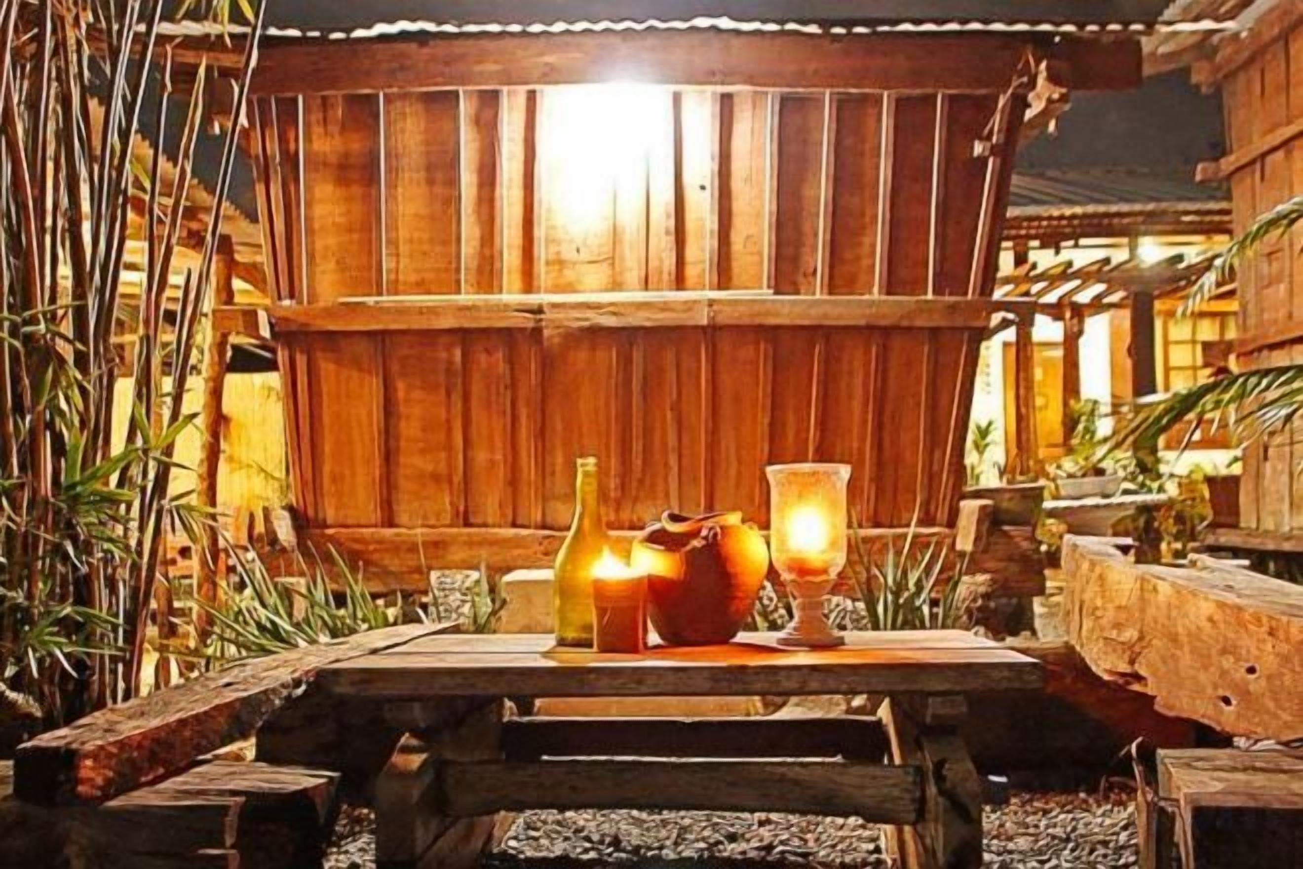 Une table en bois, ornée d’une bougie, d’une bouteille et d’un verre, dans un cadre extérieur rustique.