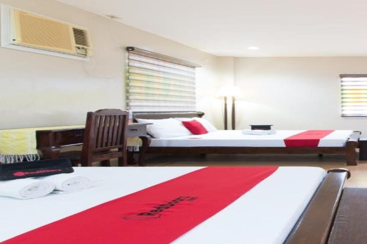 A hotel room with two beds, a desk, a chair, a window with blinds, and a door.