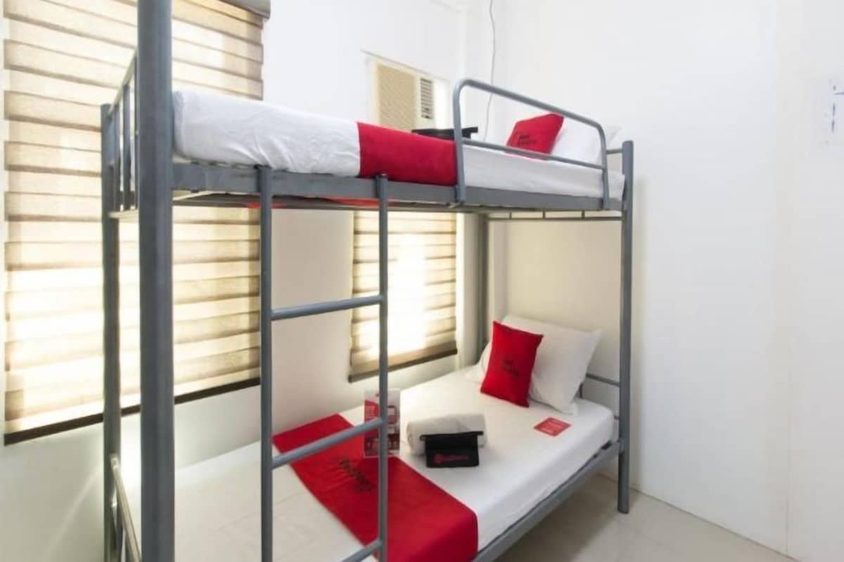 A bunk bed with a white mattress, red pillows, and a small black object on the lower bunk.