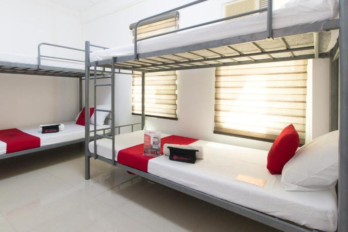 A bunk bed room with a ladder, a window with blinds, and a red pillow on each bed.