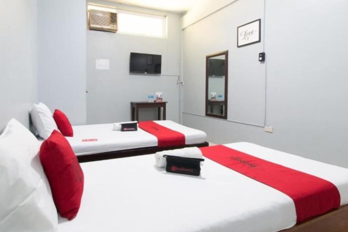A hotel room with two beds, a small table, a TV, and a mirror.