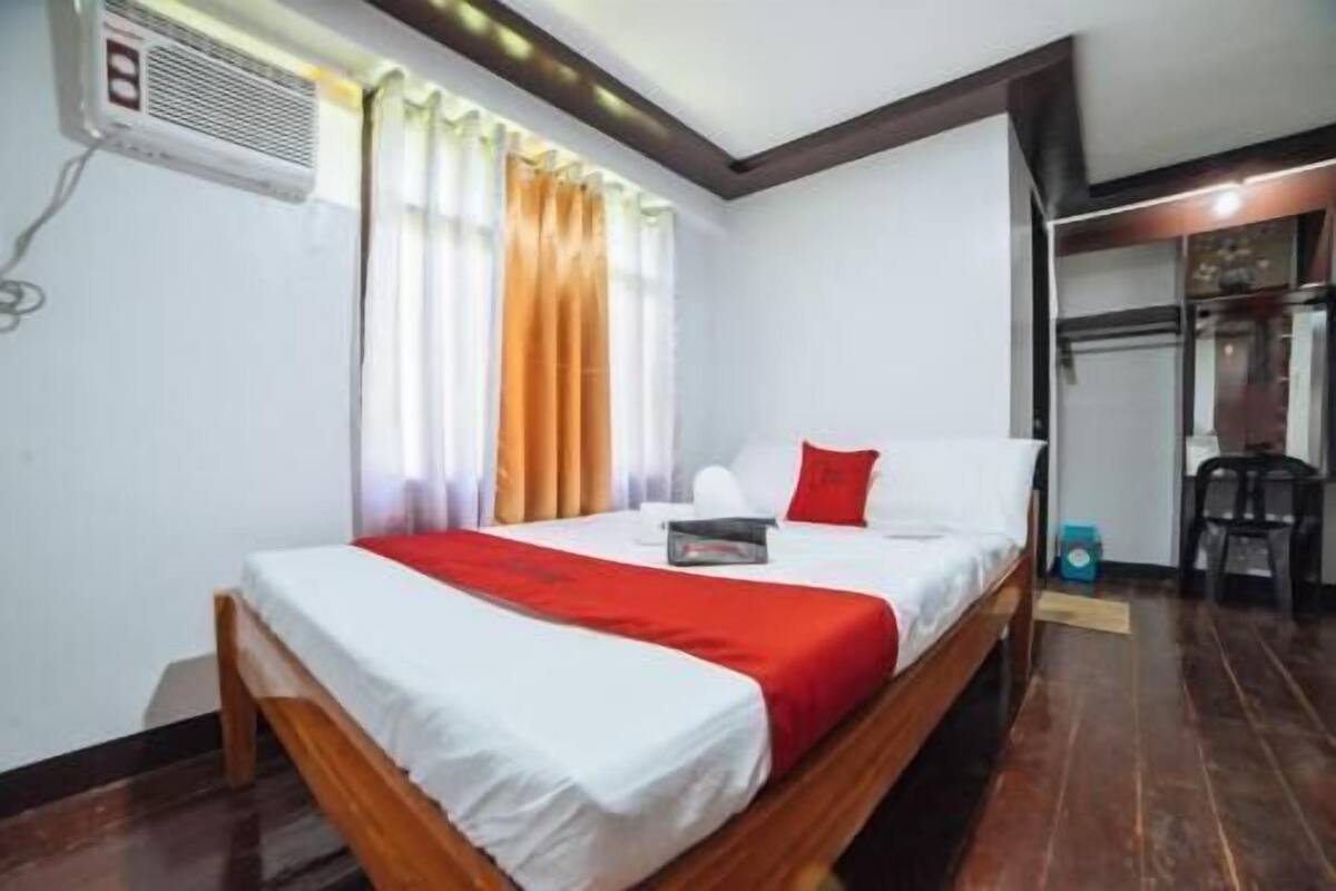 Un dormitorio con cama, cortinas, una silla y una mesita.