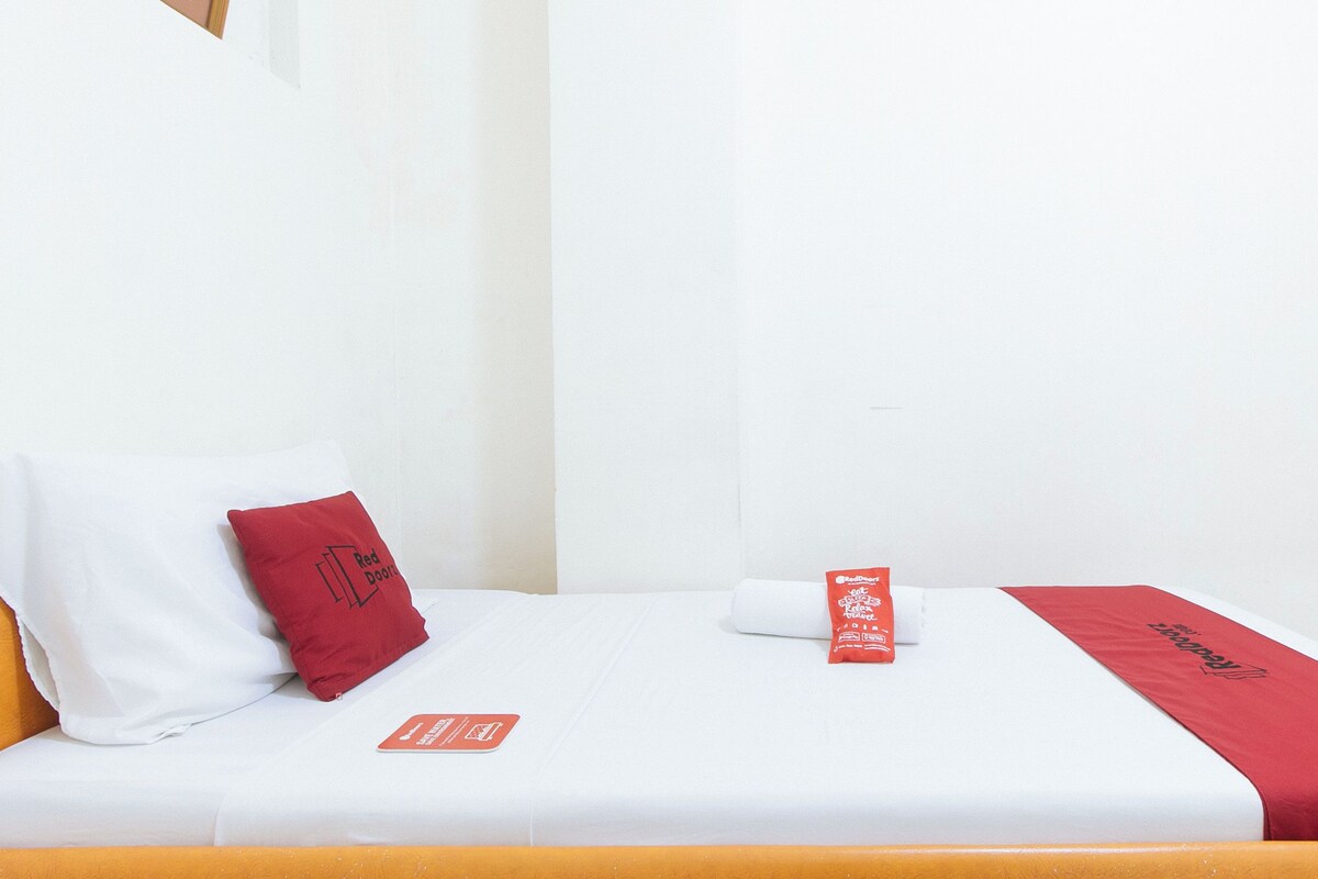 Une chambre d’hôtel avec un lit, un oreiller rouge, une couverture rouge et un panneau rouge posé sur le lit.