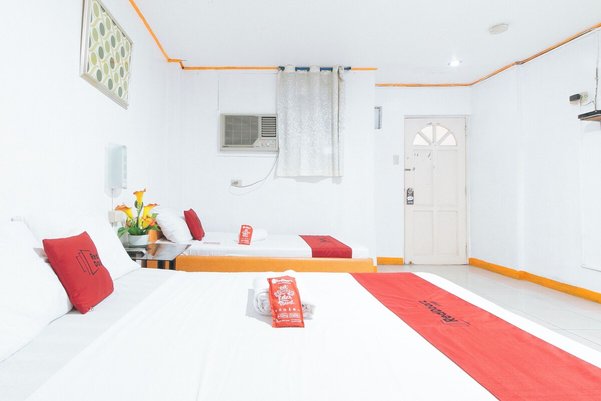 Ein Hotelzimmer mit Bett, Nachttisch, einem Fenster mit Vorhängen, einer Klimaanlage und einer Tür.