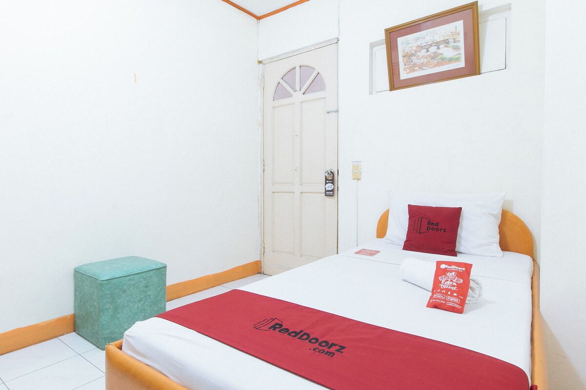 A hotel room with a bed, a door, a small stool, and a framed picture on the wall.