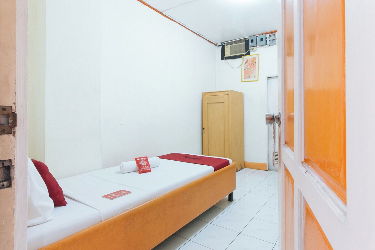 A single-bed room with a wooden wardrobe, white walls, and a tiled floor.