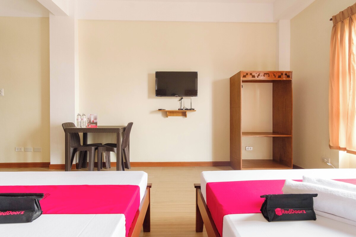A hotel room with two beds, a desk with chairs, a television on the wall, and a wardrobe.