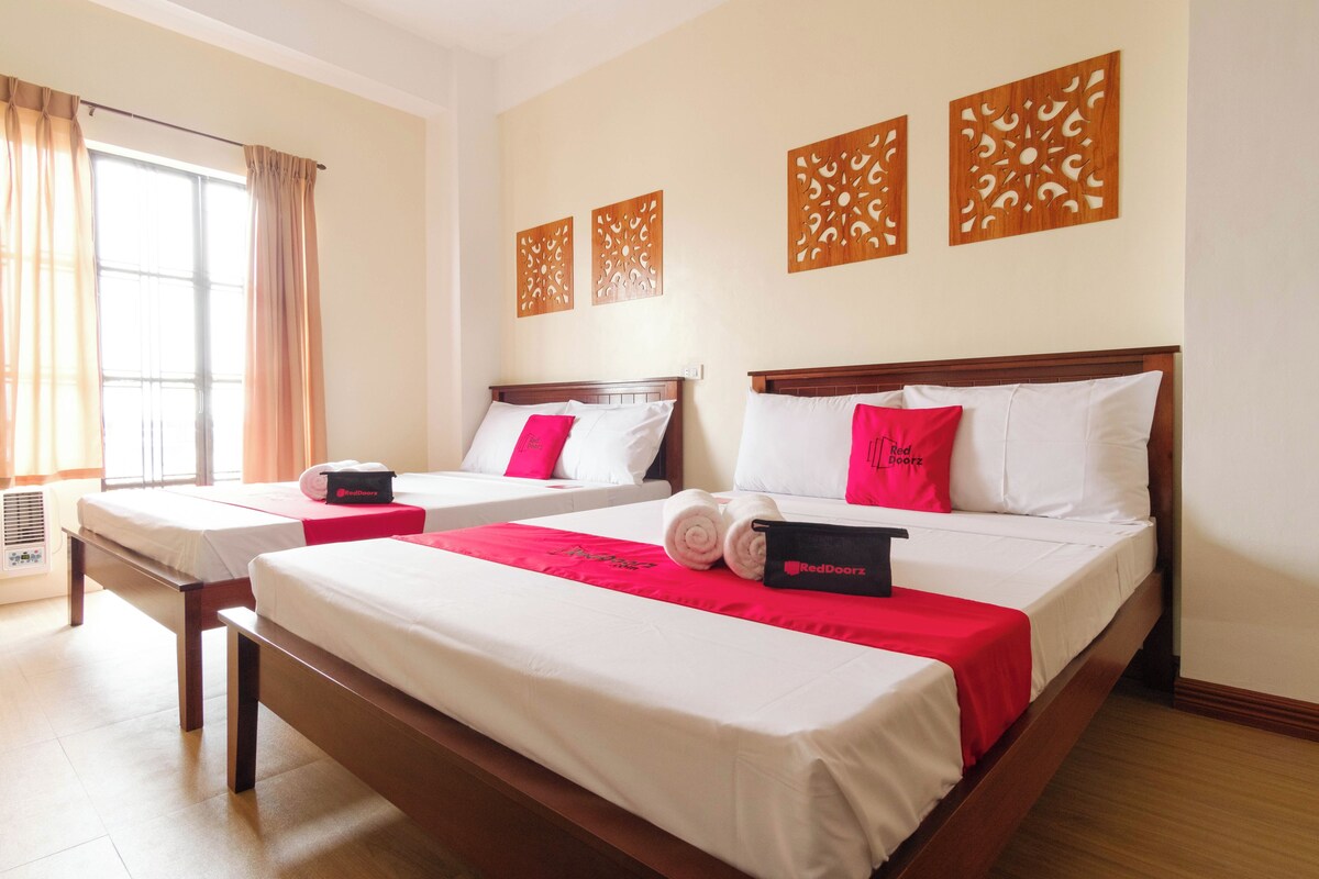A hotel room with two beds, a large window with curtains, and decorative wall panels.