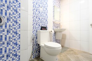 A bathroom with a white toilet, a sink, and a tiled wall with a blue and white pattern. - RedDoorz Plus @ West Nautical Road Puerto Galera (Puerto Galera)