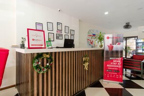 A hotel reception desk with framed certificates, a laptop, and a RedDoorz promotional banner. - RedDoorz Plus @ West Nautical Road Puerto Galera (Puerto Galera)