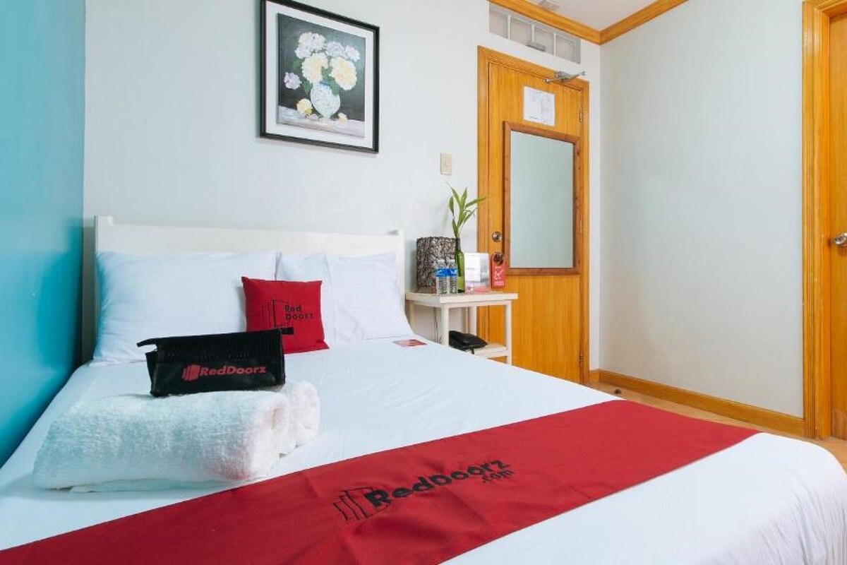 A hotel room with a bed, a bedside table, a mirror, and a wooden door.