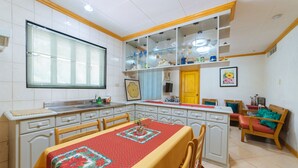 A compact kitchen with white cabinets, a dining table with a red tablecloth, and a built-in shelf with glassware. - RedDoorz @ Arimbay Legazpi City - Hostel (Legazpi)