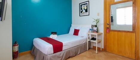 A bedroom with a bed, a bedside table, a mirror, a door, and a fire extinguisher.