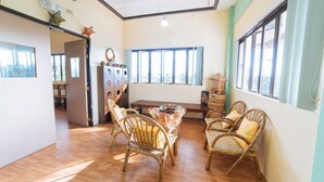 A dining area with wicker chairs, a wooden table, and a view of the outdoors through large windows. - RedDoorz @ Arimbay Legazpi City - Hostel (Legazpi)