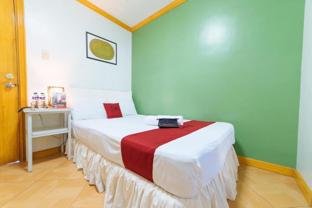 A neatly made bed with white and red bedding, a small bedside table with a lamp, and a green wall.