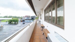 A covered outdoor area with a bench, a view of a parking lot, and a building with large windows. - RedDoorz @ Arimbay Legazpi City - Hostel (Legazpi)
