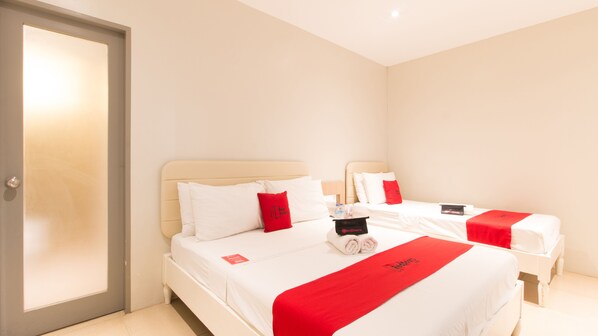 Une chambre d’hôtel avec deux lits, chacun agrémenté de draps blancs et de touches de rouge, notamment des oreillers et une couverture. Il y a une porte sur la gauche et une petite table sur laquelle se trouvent une bouteille et un objet rouge.
