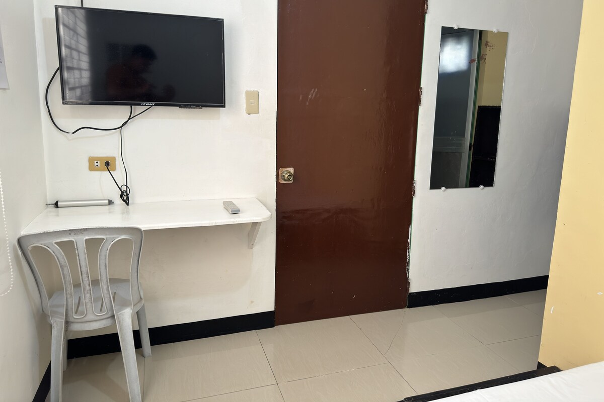 A room with a television mounted on the wall, a door, a small window, and a chair.