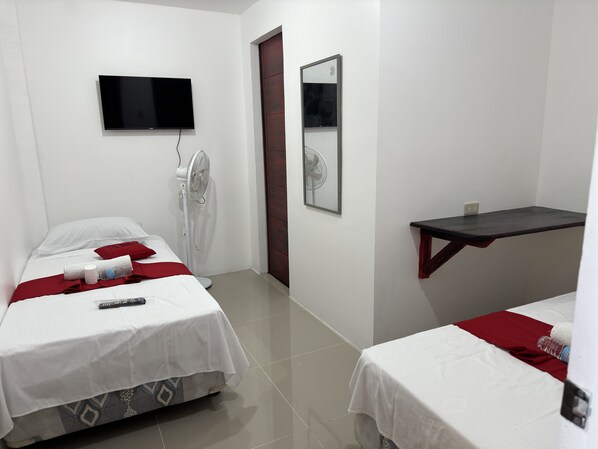 A hotel room with two beds, a TV, a fan, and a small table. - RedDoorz near Mariners Legazpi (Legazpi)