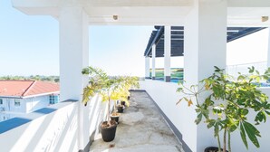Un balcon agrémenté de plantes en pot, un sol en béton et une vue sur des bâtiments en arrière-plan.