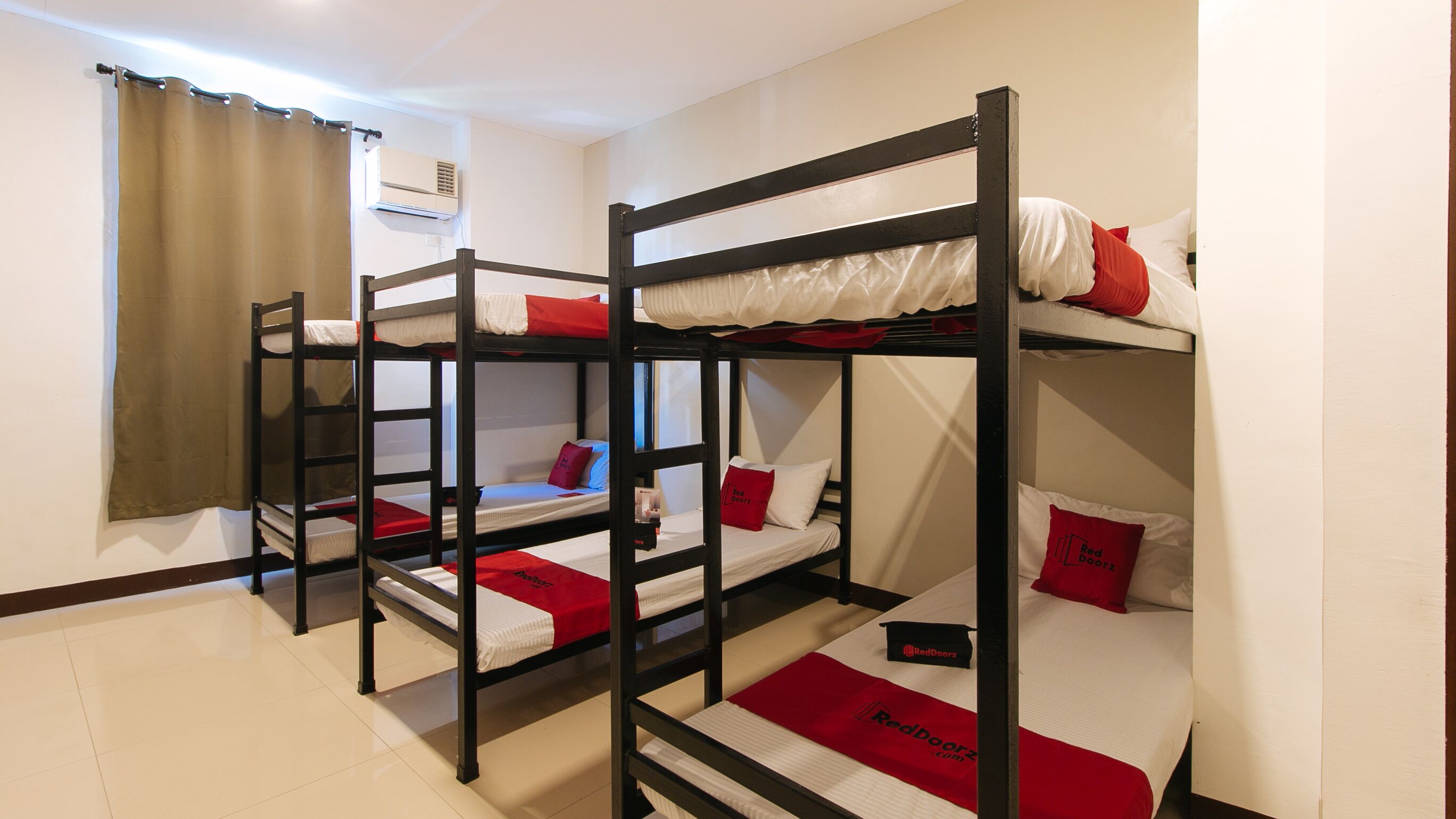A bunk bed room with three beds, each with red and white bedding, and a red and white blanket on the floor.
