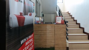 A hotel reception area with a wooden counter, a staircase, and a large poster advertising RedDoorz. - RedDoorz @ Golite Washington - Hostel (Legazpi)
