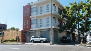 A multi-story building with a garage door, a parked white SUV, and a tree in front. - RedDoorz @ Golite Washington - Hostel (Legazpi)
