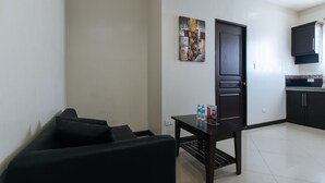 A compact living space with a dark-colored sofa, a small table with water bottles, a dark door, and a kitchen area with cabinets and a countertop. - RedDoorz @ Golite Washington - Hostel (Legazpi)