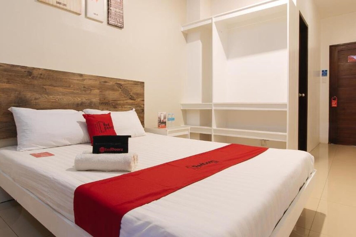 Ein Hotelzimmer mit einem Bett, einem Holz-Kopfteil, einer roten Tagesdecke und einem RedDoorz Schild.