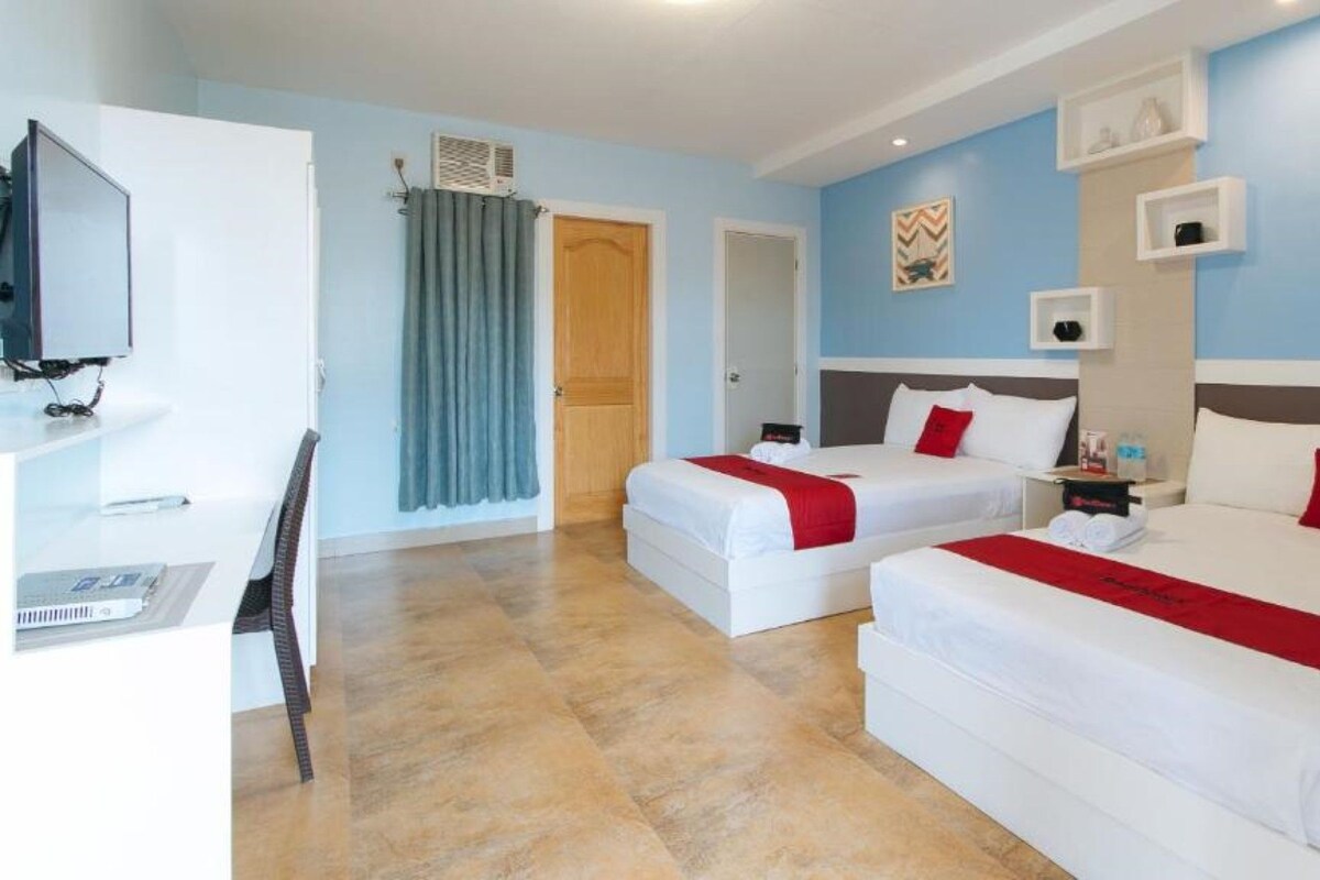 A hotel room with two beds, a desk, a TV, and a shower area.