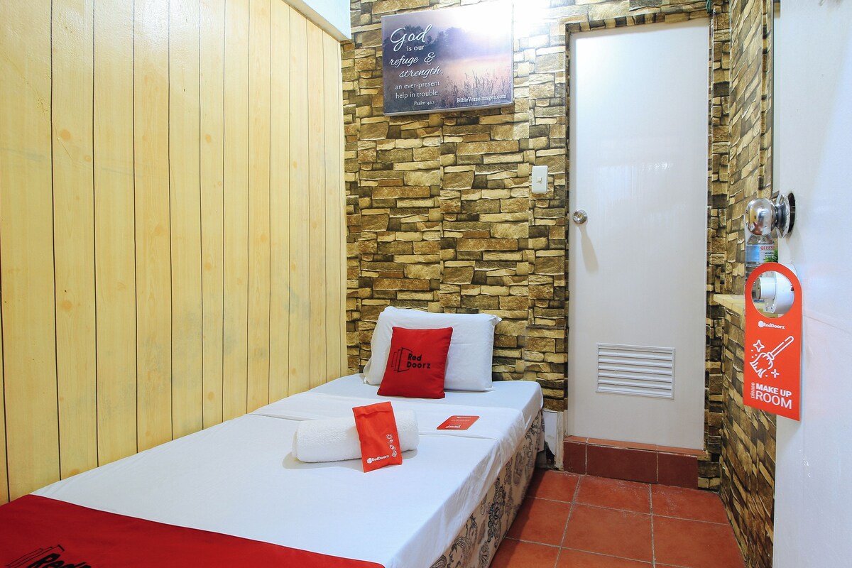 A small, single-bed room with a wooden wall, a stone wall, and a door with a Red Door sign.