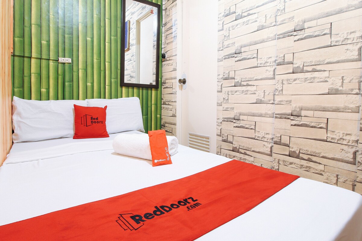 A hotel room with a bed, green headboard, stone wall, and a RedDoorz logo on the bedspread.