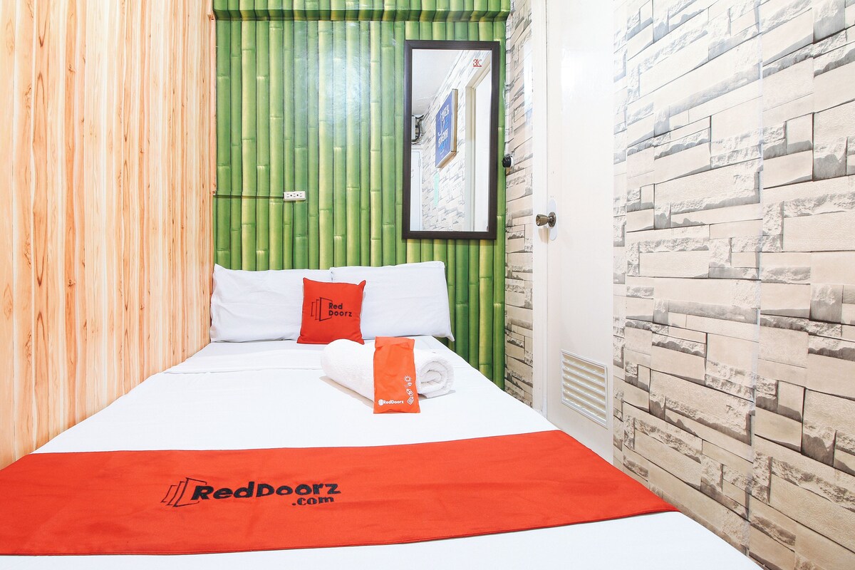 Habitación de hotel con cama, pared de bambú verde, pared de ladrillo blanco y toalla de RedDoorz.com.