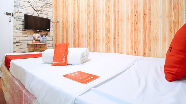 A hotel room with a bed, a TV mounted on a stone wall, and a wooden panel wall. - RedDoorz near OWWA Pasay (Pasay)