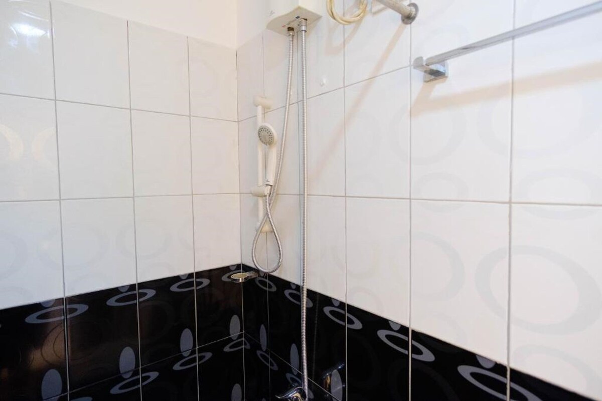 Een badkamer met betegeling in wit en zwart, een douche met handdouche en een handdoekrek.