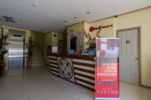 Zona de recepción de hotel con un letrero de RedDoorz, un reloj y una escalera.