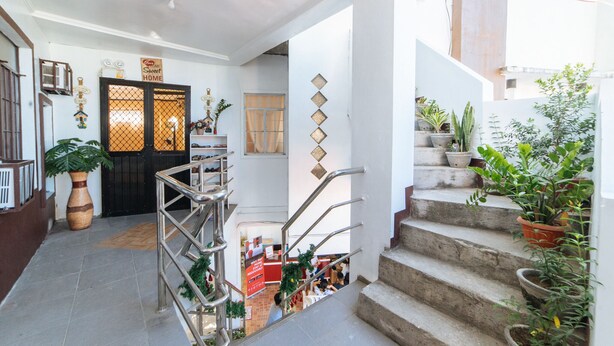 A multi-level interior with a staircase, potted plants, and a reception area with a sign.