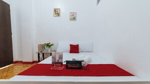A neatly made bed with a red pillow, a small table with a plant, and a RedDoorz bag on the bed.