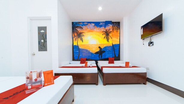 A hotel room with two single beds, a large painting of a sunset over water, a television on the wall, and a door with a decorative glass panel. - RedDoorz @ Bonifacio Extn Baler (Baler)