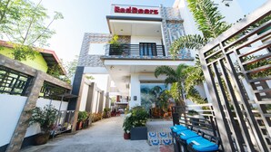 A modern building with a 'RedDoorz' sign, featuring a balcony, potted plants, and outdoor seating. - RedDoorz @ Bonifacio Extn Baler (Baler)