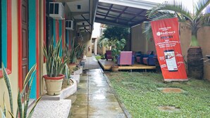 A hotel corridor with potted plants, a RedDoorz promotional banner, and outdoor seating. - RedDoorz @ Bankal Lapulapu (Lapu-Lapu)